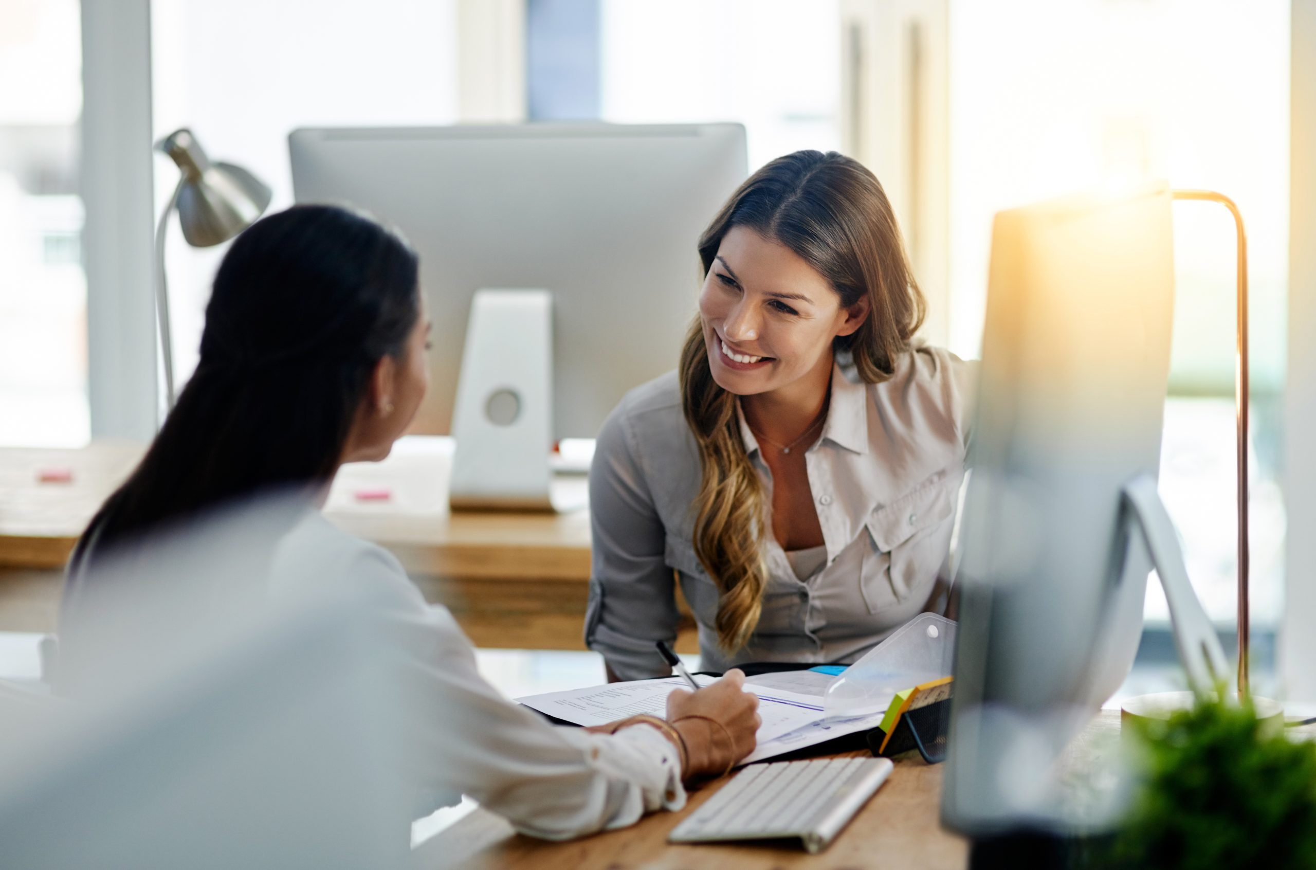 Shot of two young businesswomen talking to each other while being seated in the office at work. - Flex blog image